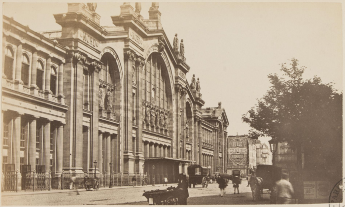 Photo historique de la façade de la Gare du Nord vers 1870. Vendeur de rue au premier plan. On aperçoit également quelques diligences tractées par des chevaux.