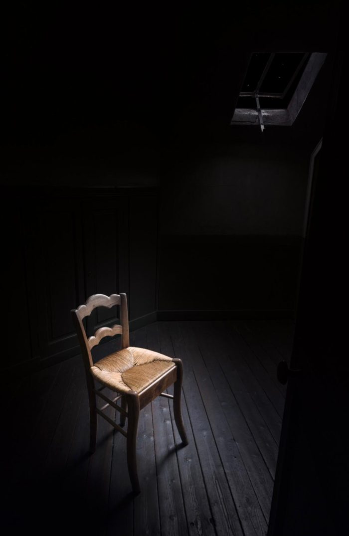 Chaise en bois et paille tressée, dans la pénombre d'une pièce mansardée, sol en parquet ancien et fenêtre de toit entre-ouverte