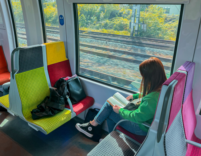 Une voyageuse assise dans un train de la ligne H, à côté d'une fenêtre, un livre à la main