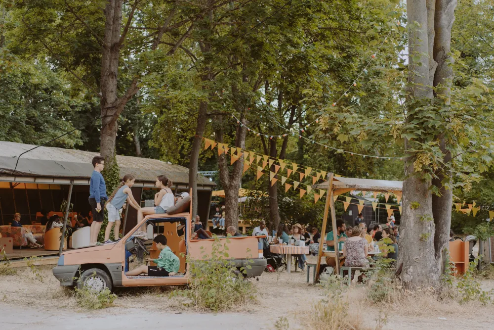 Photo de festivités en après-midi.
Une carcasse de voiture orange sert d'air de jeux à des enfants
