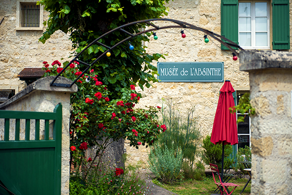 Photo du musée de l'Absinthe. La cours intérieur abrites quelques chaises et tables, on y voit un parasol rouge et un grand rosier